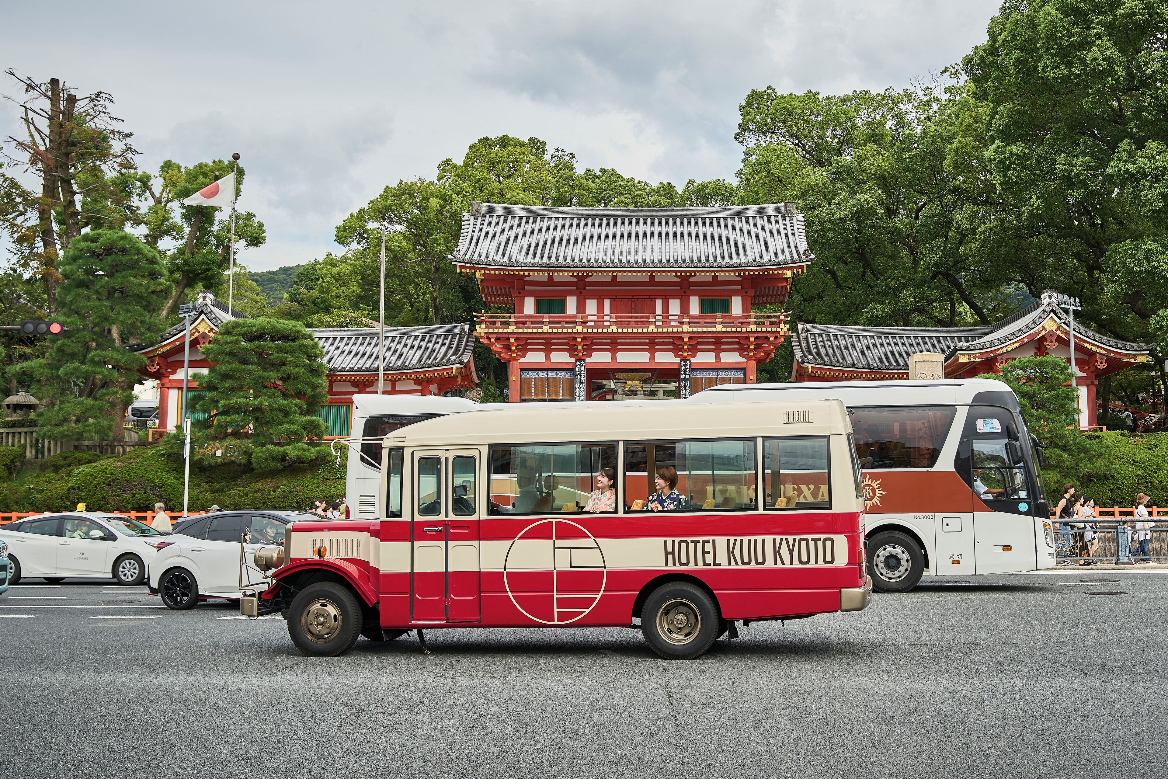 A red and white bus with 'HOTEL KUU KYOTO' written on the side, parked in front of traditional Japanese buildings.