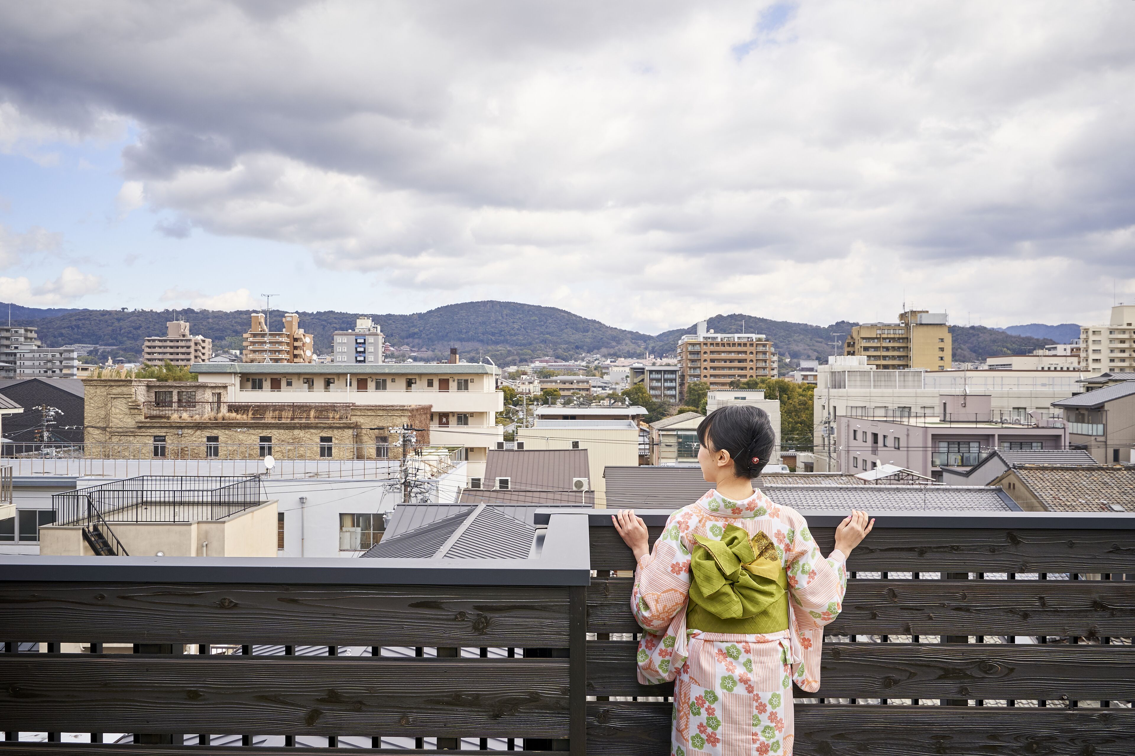 A person standing on a rooftop with a view of a cityscape and mountains in the background.