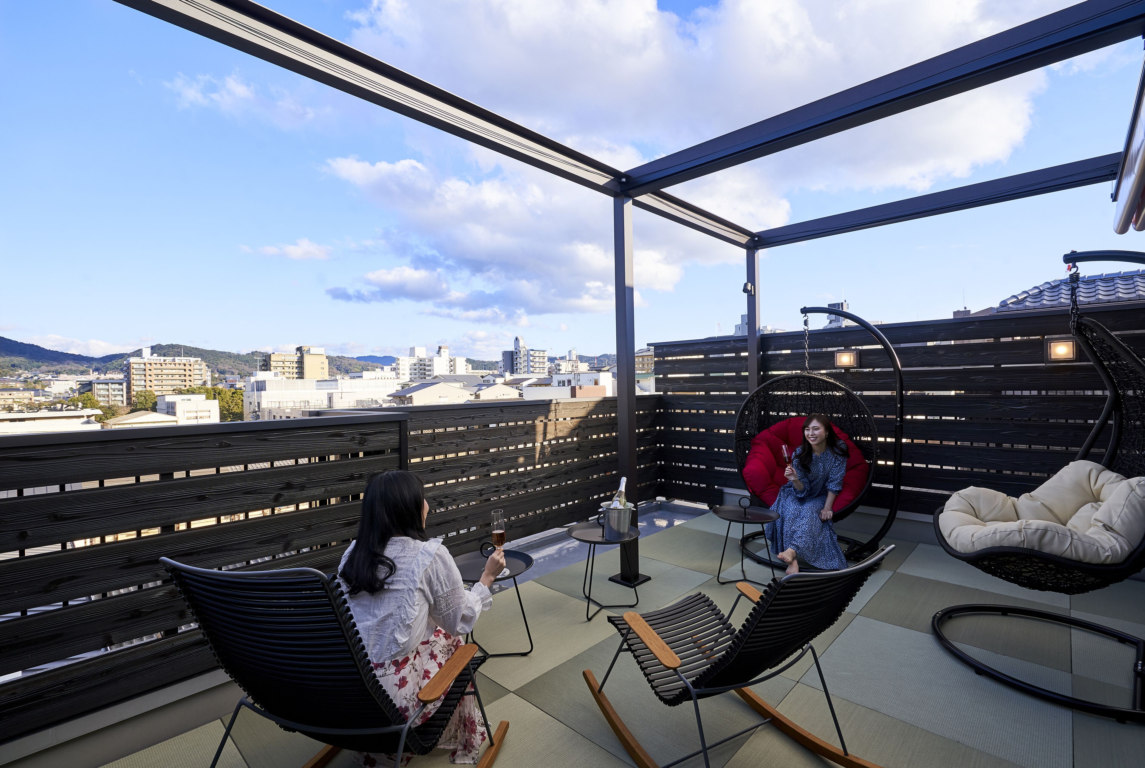A rooftop terrace with a view of the city, a wooden fence, and two rocking chairs.
