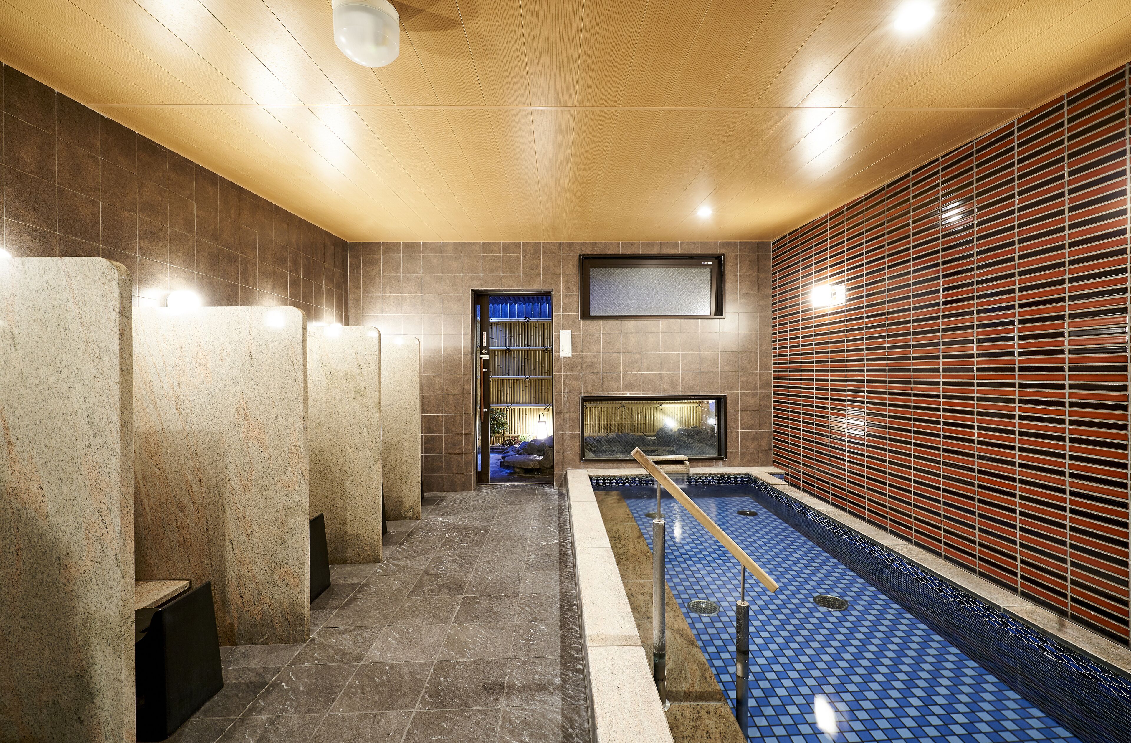 A modern indoor pool area with a tiled floor, a pool with a blue mosaic pattern, and a wooden ceiling.