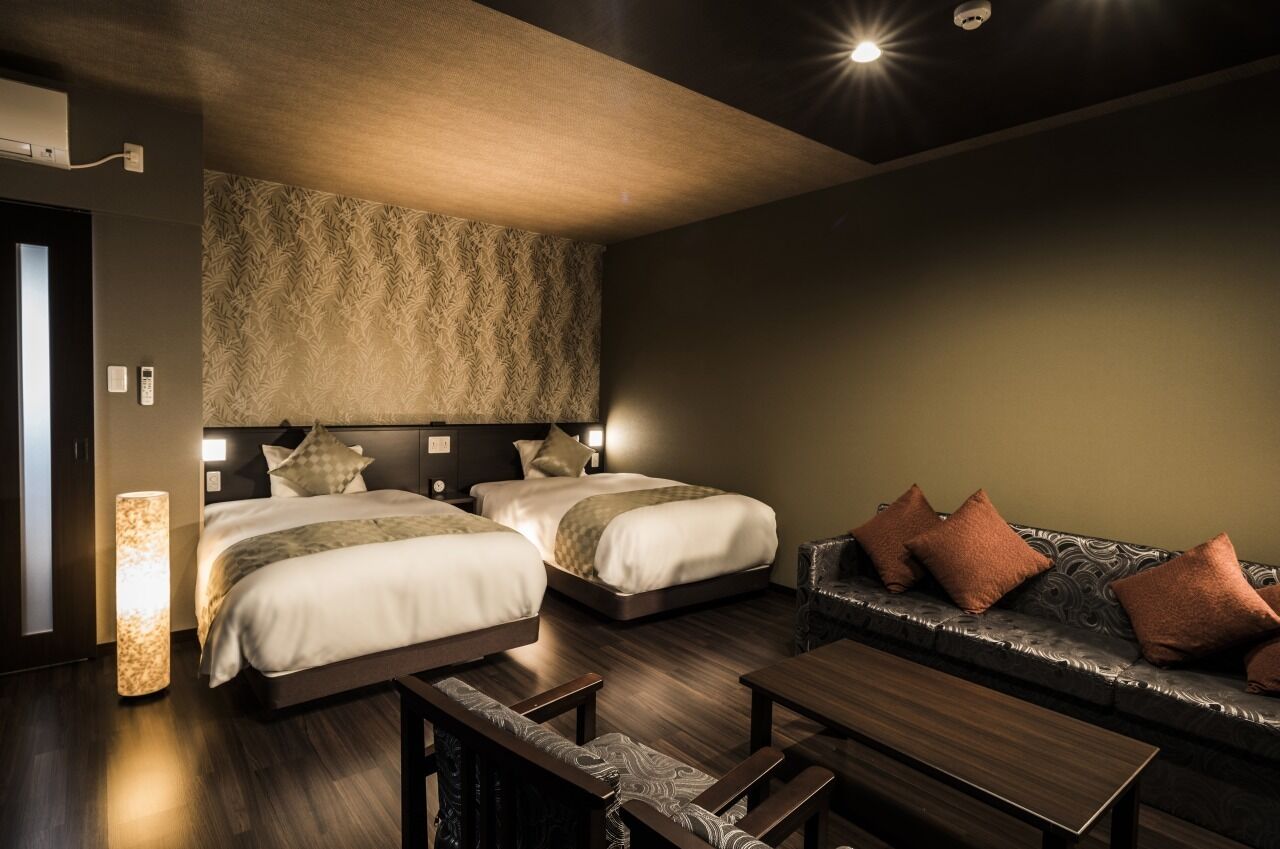 A hotel room with two beds, a sofa, a table, and a patterned wall.