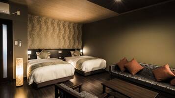 A hotel room with two beds, a sofa, a table, and a patterned wall.