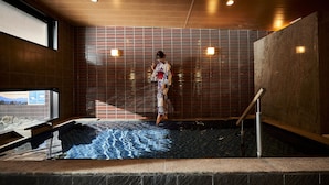 A person in a traditional Japanese yukata standing in a stone hot spring bath area with wooden slats and a tiled floor. - Hotel Kuu Kyoto (Kyoto)