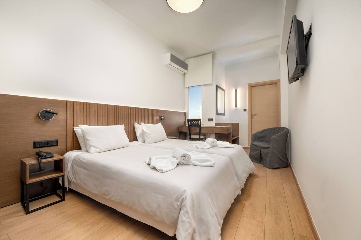 A hotel room with a large bed, a desk, a chair, a TV mounted on the wall, and a wooden headboard.