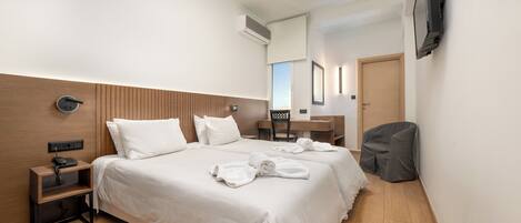 Habitación de hotel con una cama grande, un escritorio, una silla, un televisor montado en la pared y un cabecero de madera.