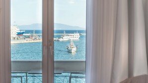 Vista desde una habitación con balcón que da a un puerto, con un gran crucero y una embarcación más pequeña.
