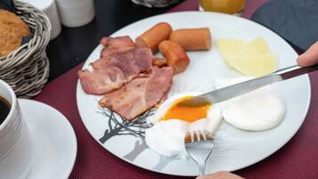 Prato de café da manhã com presunto, salsichas, queijo e um ovo frito.