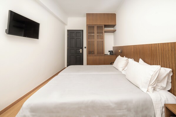 A modern hotel room with a large bed, a flat-screen TV mounted on the wall, a wooden headboard, and a built-in wardrobe. - Hotel Lesvion (Lesvos)