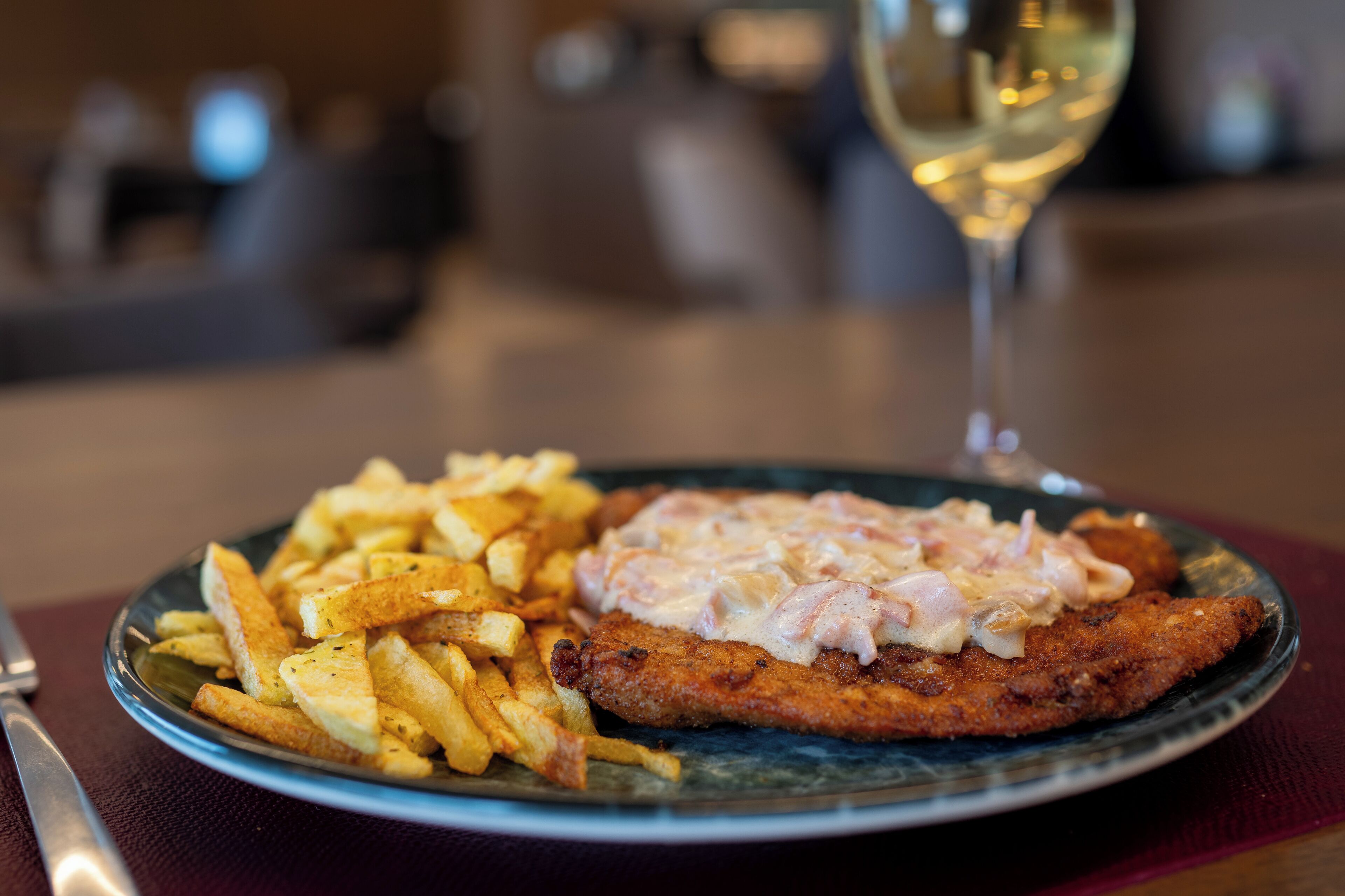 A plate of food with fries and a breaded cutlet, accompanied by a glass of white wine.