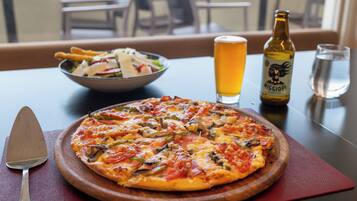 A pizza on a wooden board, a beer bottle, a glass of beer, and a bowl of salad on a table.