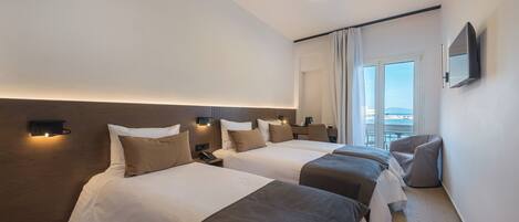 A hotel room with two beds, a TV, a bedside table, a lamp, and a window with curtains.