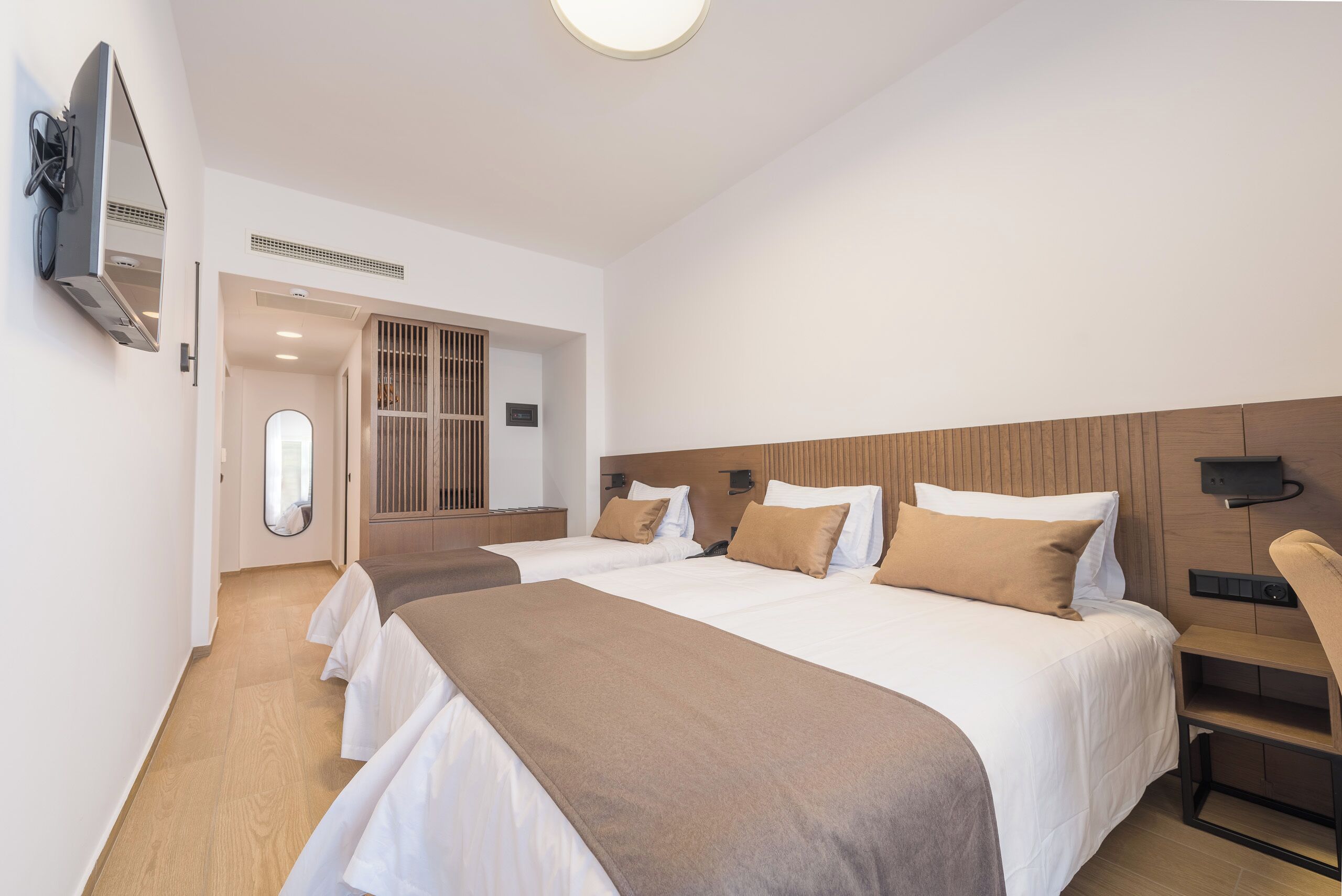 Een hotelkamer met twee bedden, een aan de muur bevestigde televisie, een houten hoofdbord en een kleine tafel.
