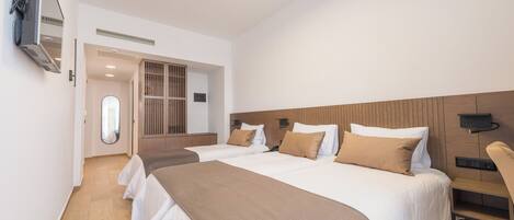 A hotel room with two beds, a TV mounted on the wall, a wooden headboard, and a small table.