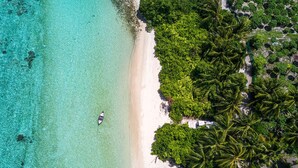 Vue aérienne d’une plage aux eaux turquoise et limpides, bordée d’un rivage sablonneux et d’une végétation tropicale luxuriante.
