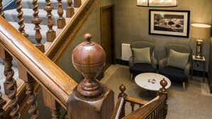 A staircase with wooden balusters leading to a room with two armchairs, a small table, and a lamp. - Kinnettles Hotel and Spa (St. Andrews)