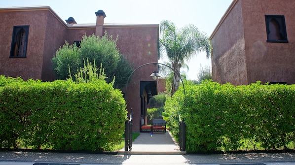 A pathway leading to a building with a traditional architectural style, surrounded by well-maintained hedges.