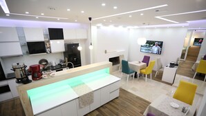 A modern kitchen with a central island, a dining area with colorful chairs, and a flat-screen TV mounted on the wall. - HOTEL LIBRIS boutique (Sarajevo)