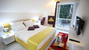 A hotel room with a bed, nightstand, lamp, TV, and a window with a view of trees. - HOTEL LIBRIS boutique (Sarajevo)