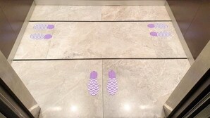 An elevator interior with a marble floor and purple directional markers. - Studio Ekamai (Bangkok)