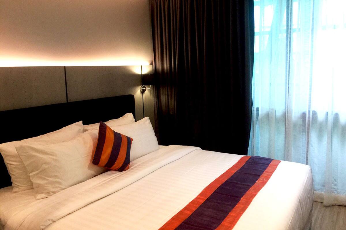 Habitación de hotel con una cama grande, cabecera, mesita de noche y ventana con cortinas.