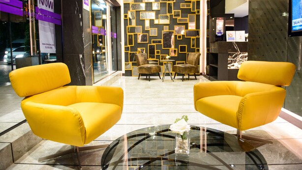 A lobby with two yellow armchairs, a glass coffee table, and a decorative wall with geometric patterns. - Studio Ekamai (Bangkok)