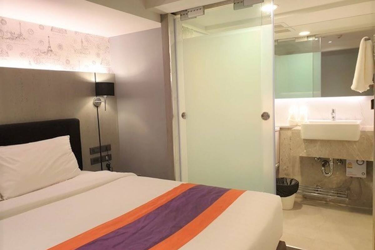 Habitación de hotel con una cama, una mesita de noche, una lámpara, una puerta corredera hacia el baño y un espejo.