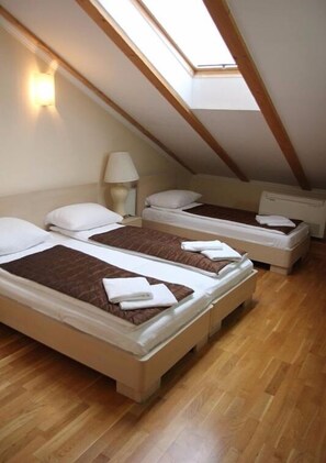 A dormitory room with three single beds, wooden flooring, and skylights. - ETN Hotel (Sarajevo)