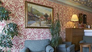 A room with patterned wallpaper, a painting, a lamp, a clock, and a sofa. - ETN Hotel (Sarajevo)