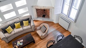 A living room with a fireplace, wooden flooring, a sofa with cushions, a coffee table, and a dining table with chairs. - Borgo San Jacopo Deluxe (Florence)
