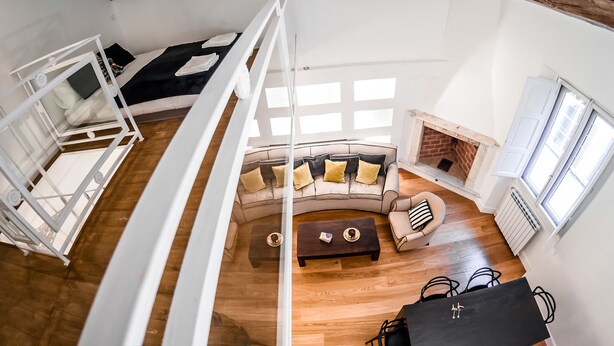 A loft-style room with a high ceiling, exposed wooden beams, a sofa set, a fireplace, and a dining table. - Borgo San Jacopo Deluxe (Florence)