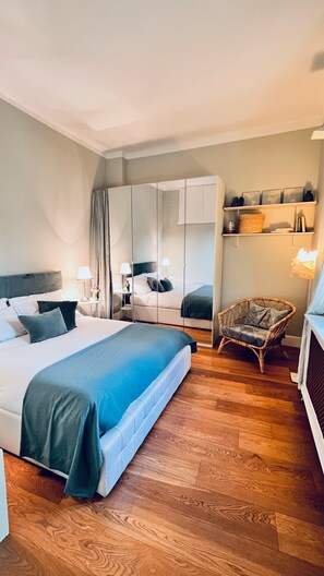 A hotel room with a large bed, a chair, a wardrobe, and a desk with a lamp.