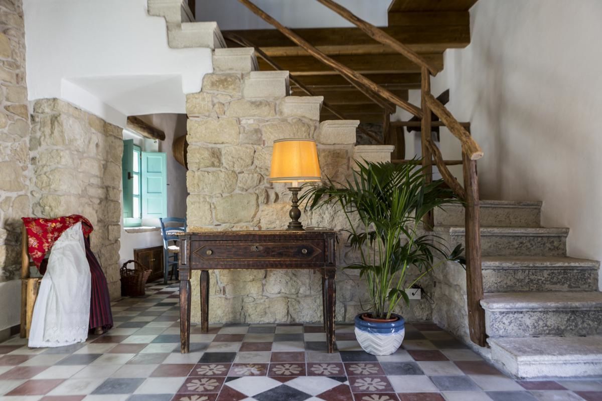 A stone staircase with a wooden handrail, a checkered floor, a table with a lamp, and a potted plant.