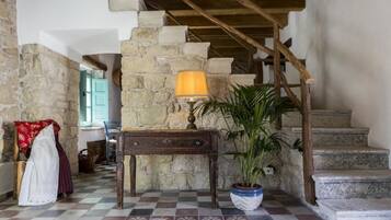 A stone staircase with a wooden handrail, a checkered floor, a table with a lamp, and a potted plant.