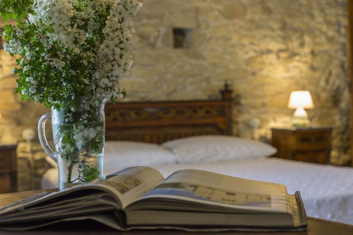 A room with a bed, a nightstand with a lamp, and a vase with flowers on a table.