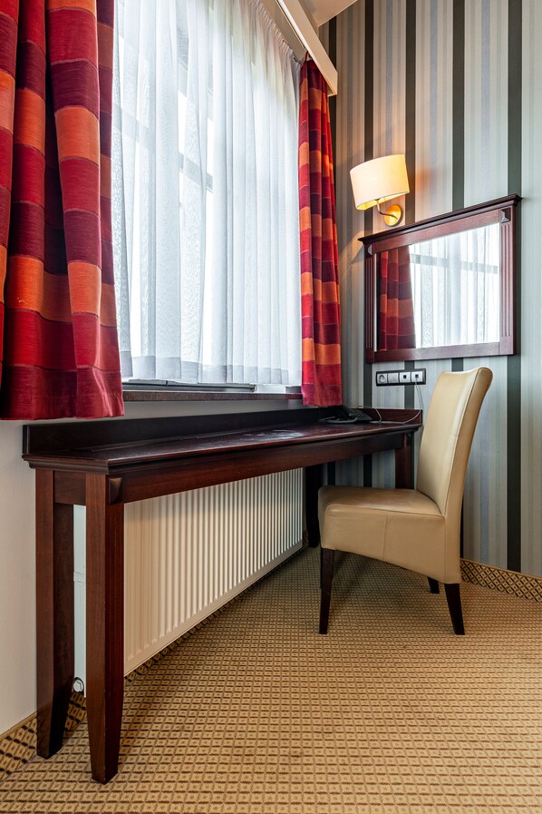A hotel room with a wooden desk, a chair, a lamp, a mirror, and striped wallpaper. - Hotel Galicja Wellness & SPA (Oswiecim)