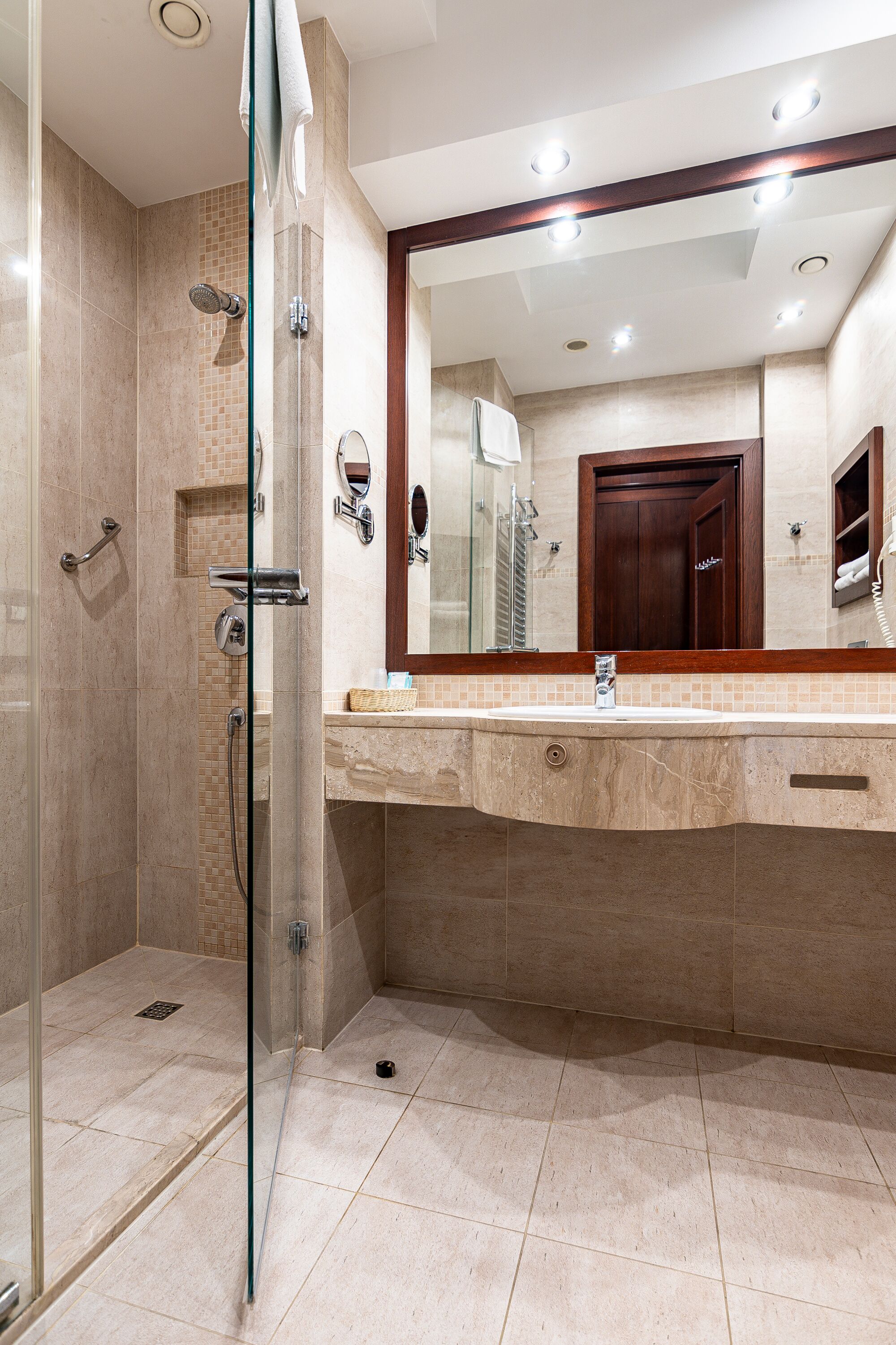 Une salle de bain moderne avec une douche à parois de verre, un grand miroir et un sol carrelé de couleur beige.