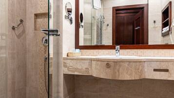 Un baño moderno con ducha de vidrio, un espejo grande y piso de baldosas color beige.