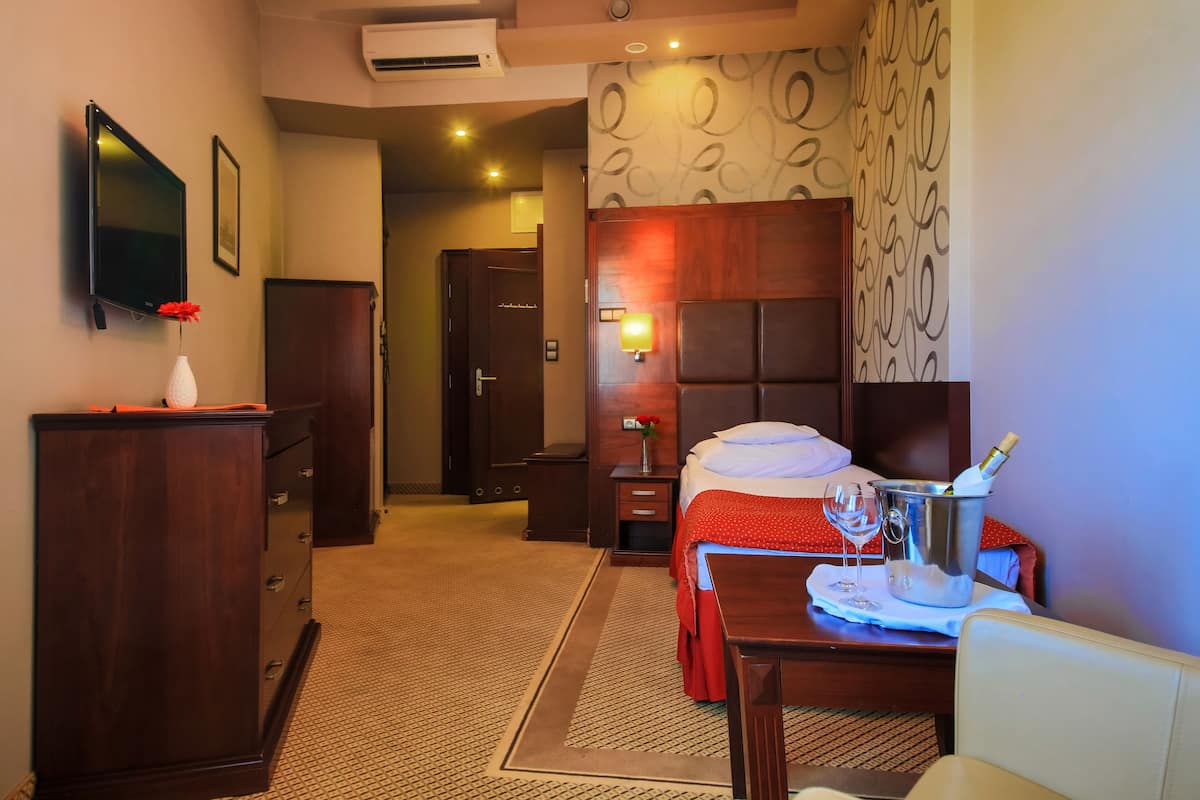 Hotelkamer met een bed, nachtkastje, televisie, kast, bureau met stoel en een behang met patroon.