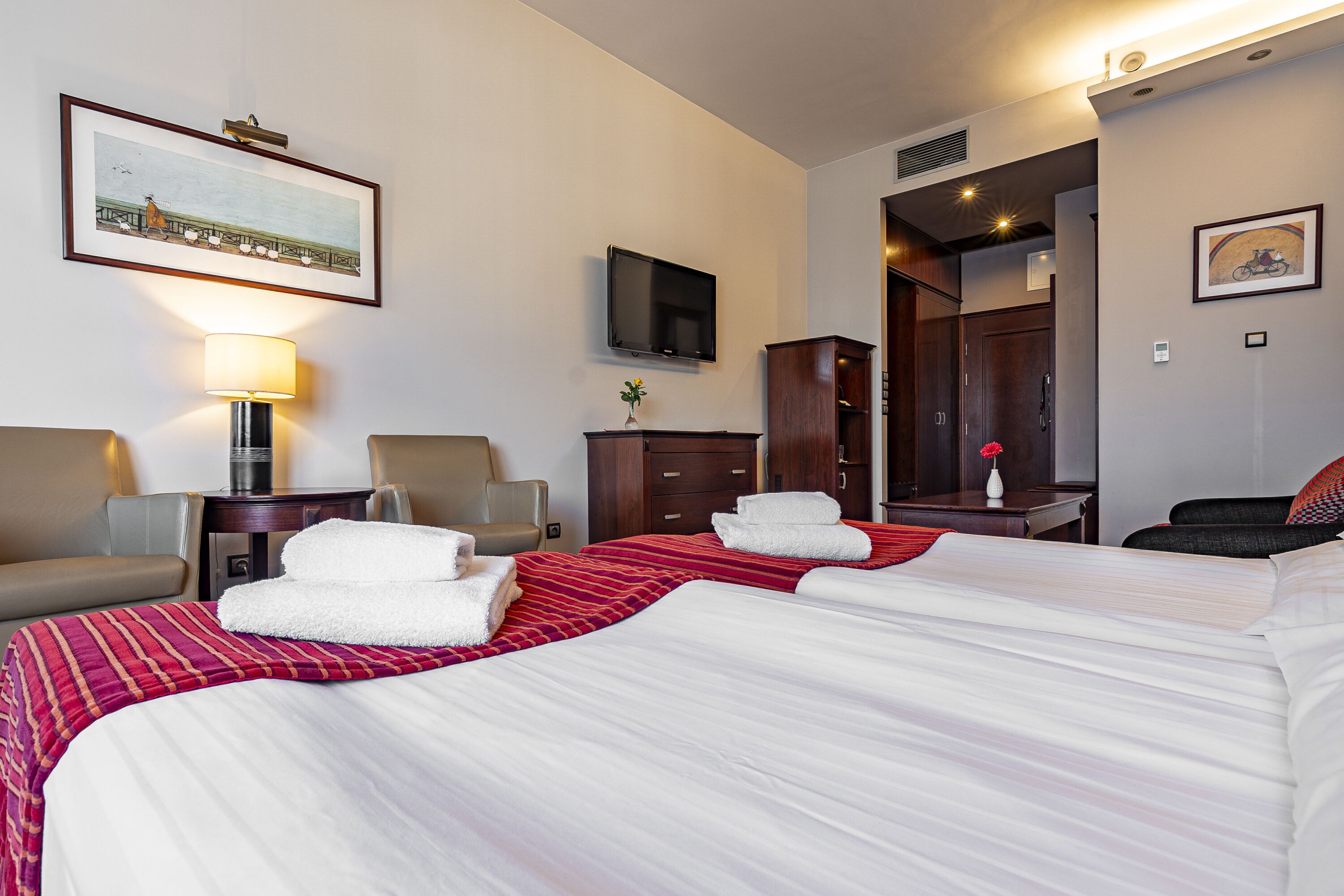 A hotel room with two beds, a TV, a desk, and a mirror.