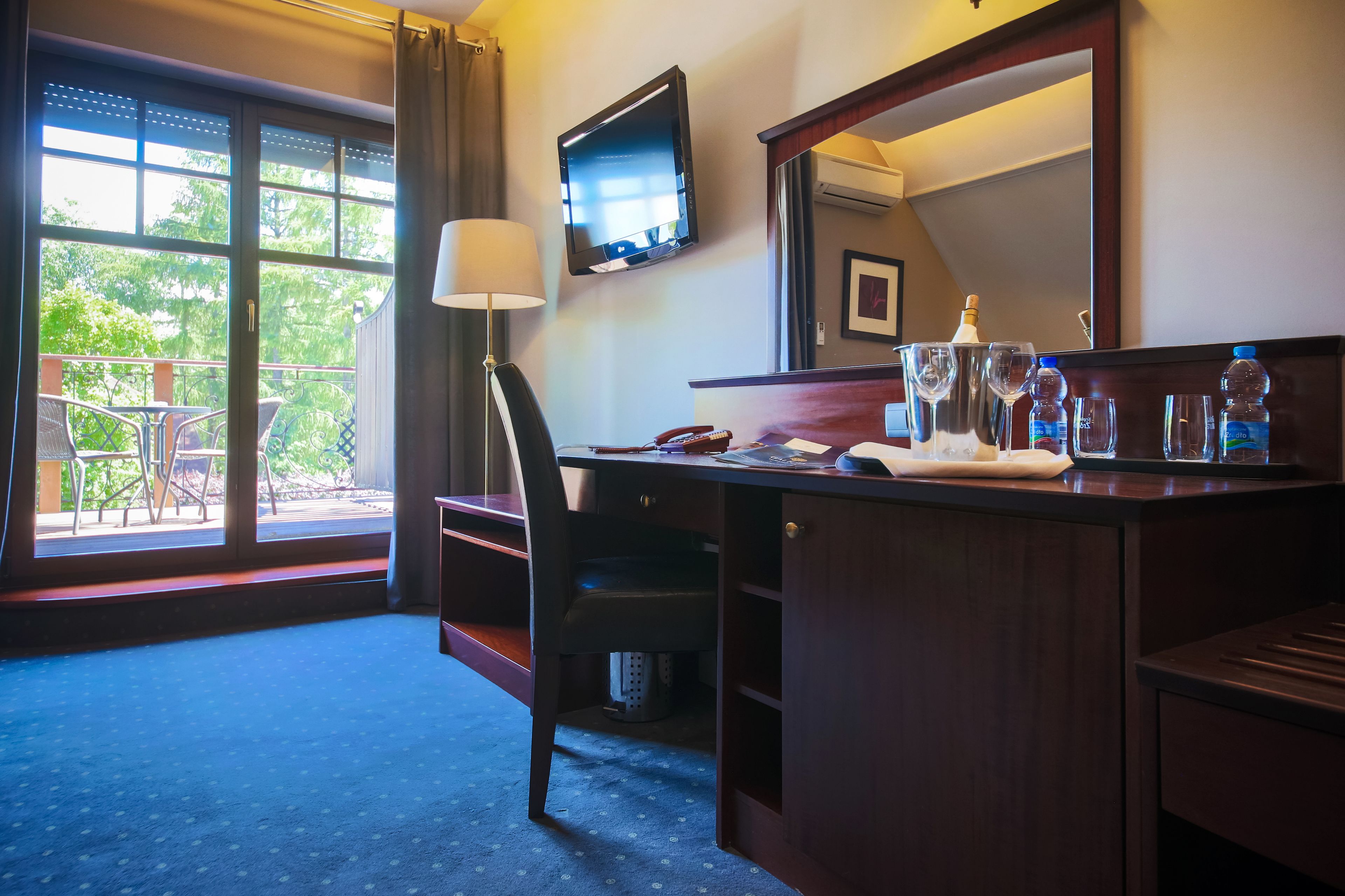 A hotel room with a desk, chair, and a large window with a view of the outdoors.