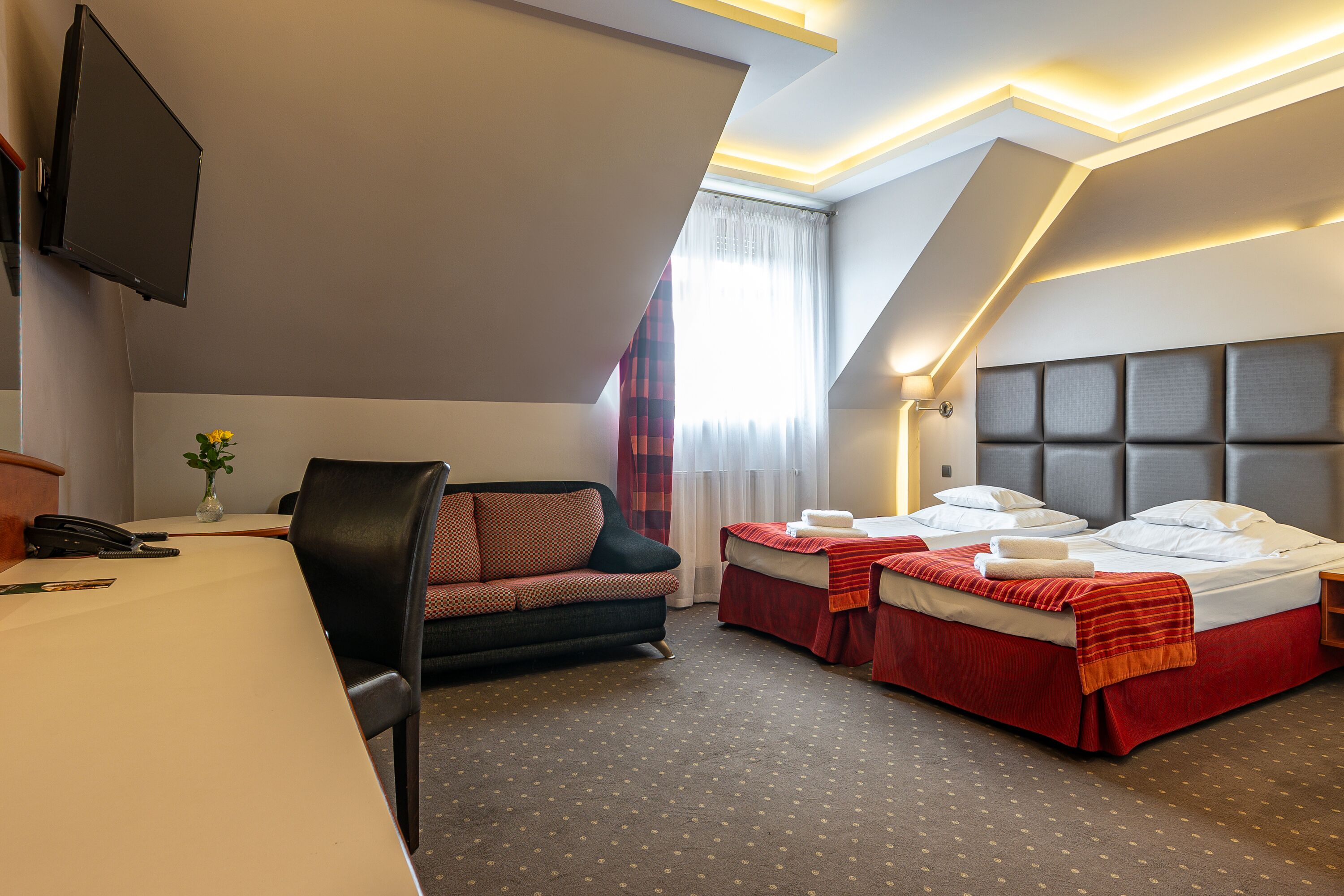 A hotel room with a desk, two beds, a sofa, and a TV.
