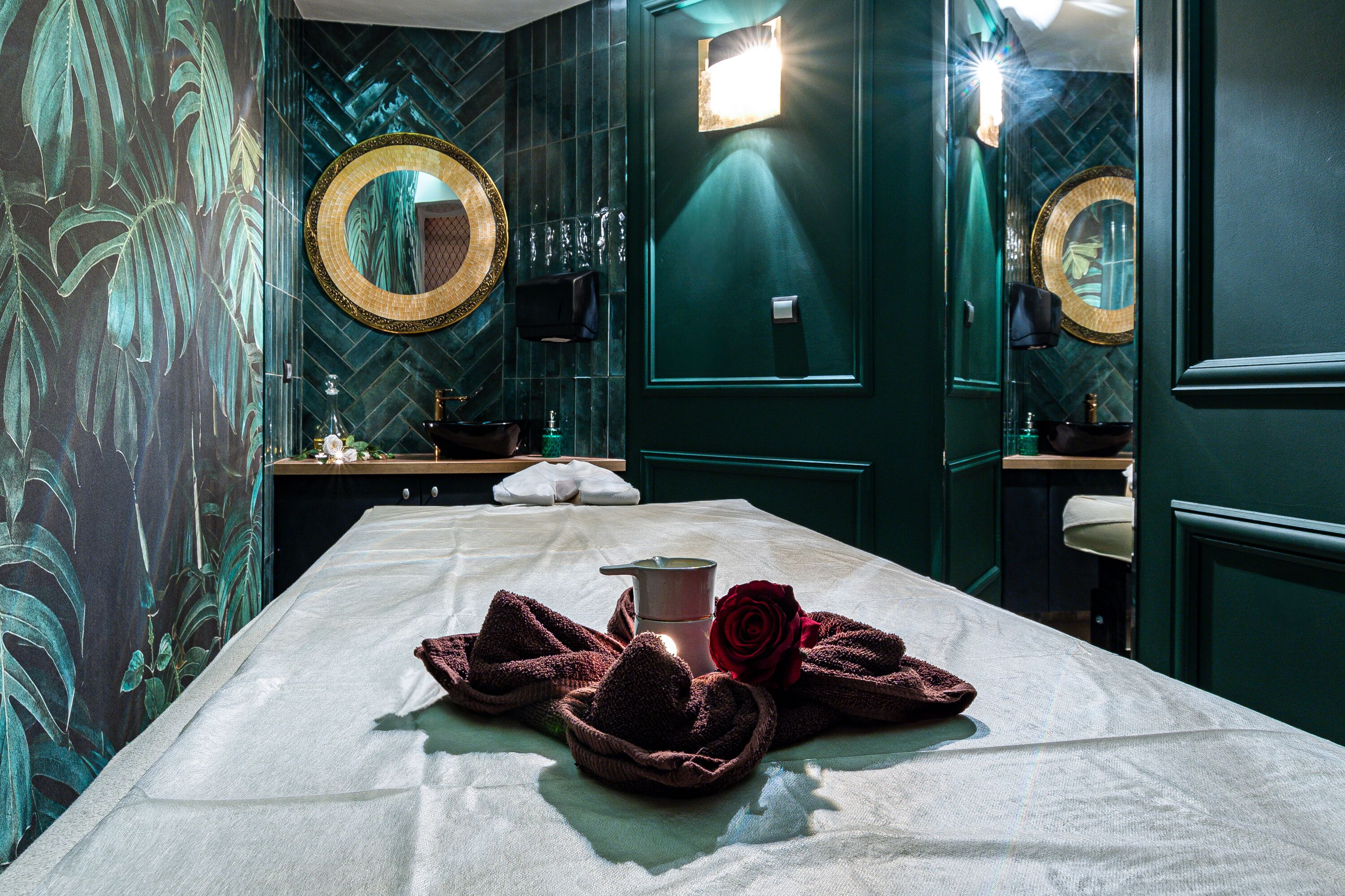 A spa room with a massage table, towels, a rose, and a mirror.
