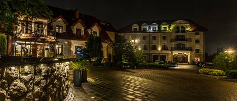 A hotel with a stone facade, a paved courtyard, and illuminated balconies.