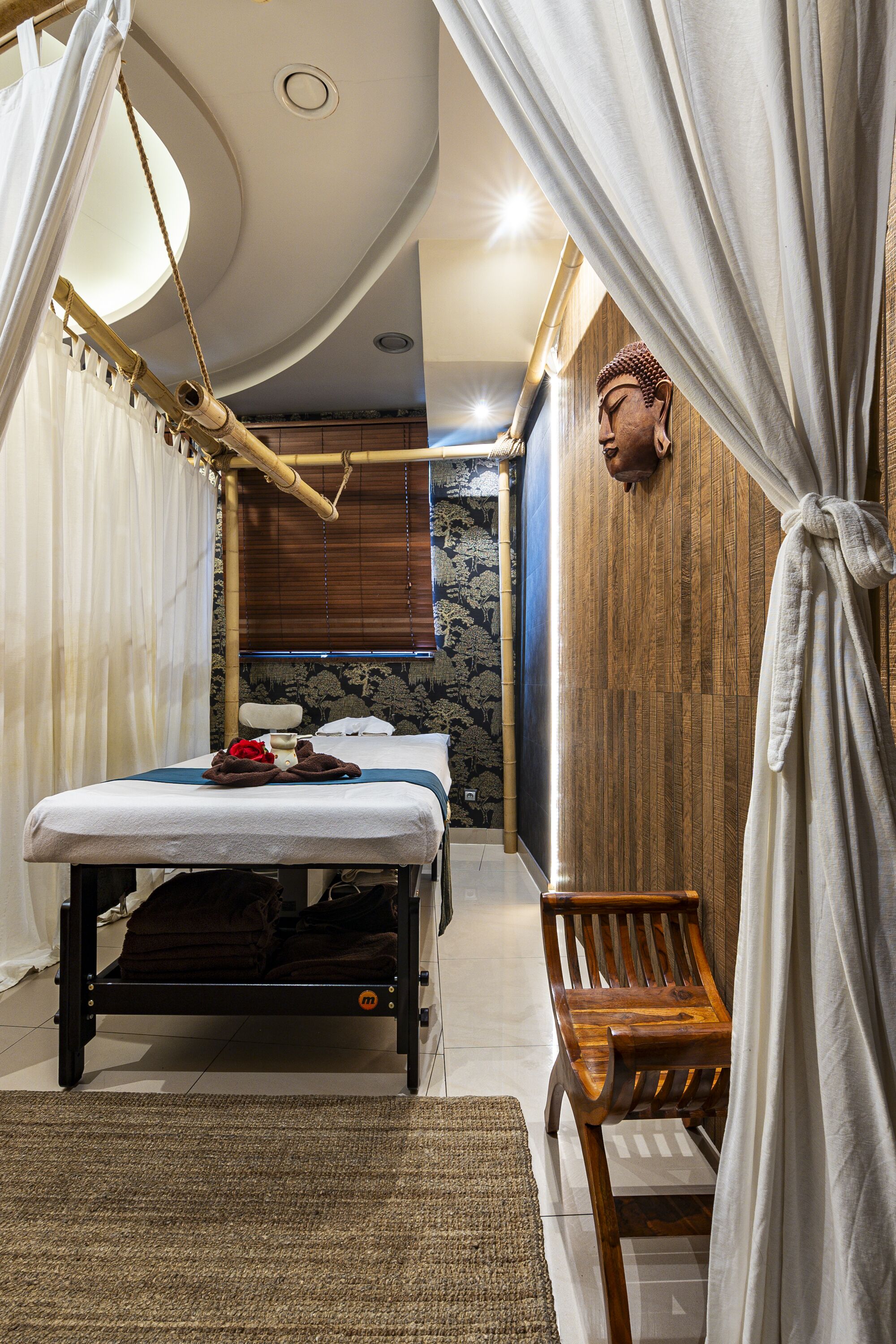 A room with a bed, a wooden bench, a hanging chair, and a large Buddha statue.