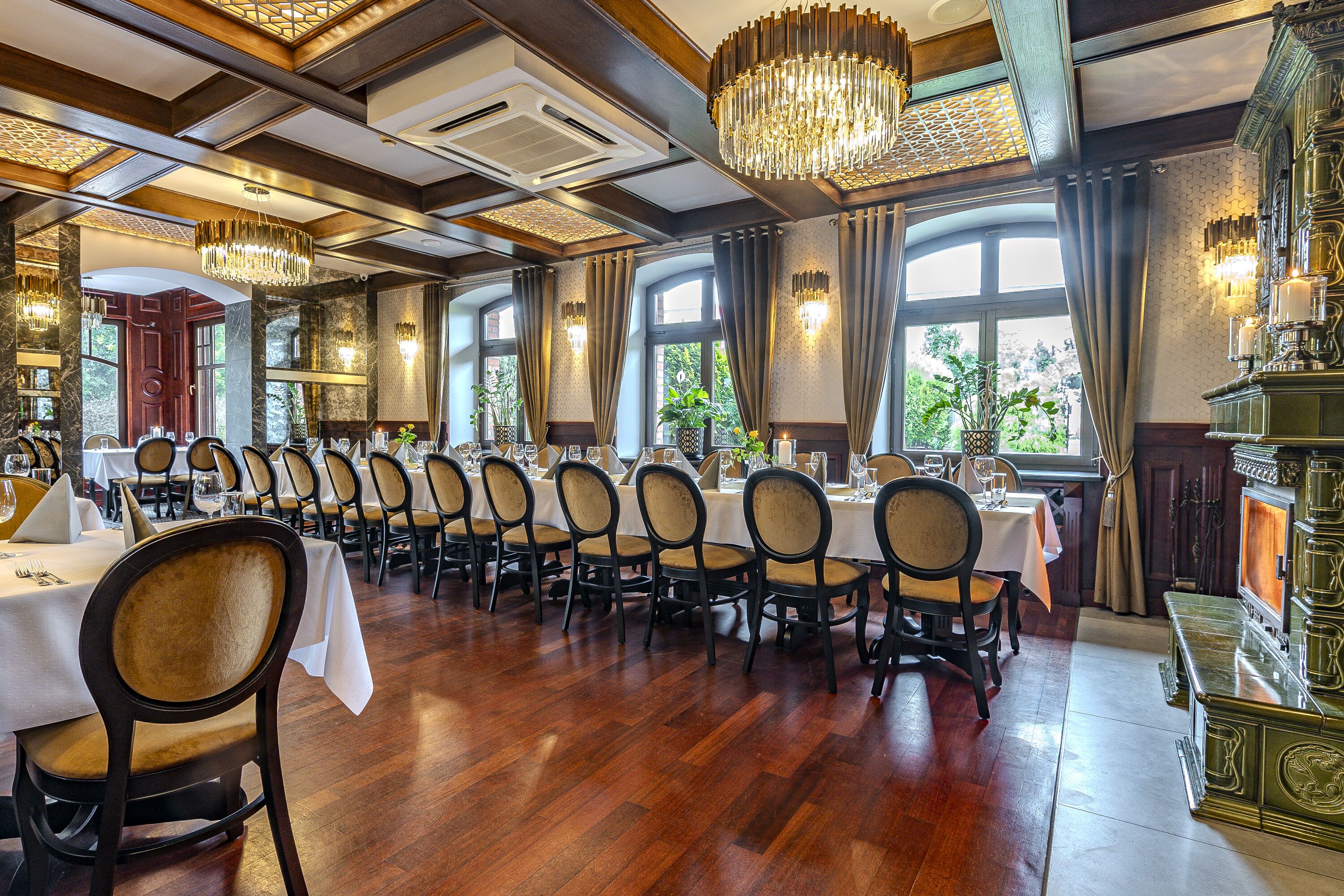 A formal dining room with wooden flooring, multiple tables set for dining, and chandeliers.