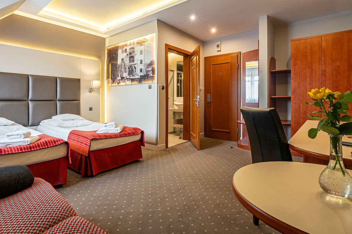 Een hotelkamer met twee bedden, een eettafel, een stoel en een vaas met bloemen.