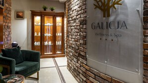 A reception area with a modern design, featuring a reception desk, a green sofa, and a wall-mounted sign for Galicja Wellness & Spa.