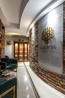 Uma área de recepção com design moderno, apresentando um balcão de atendimento, um sofá verde e uma placa na parede para Galicja Wellness & Spa.