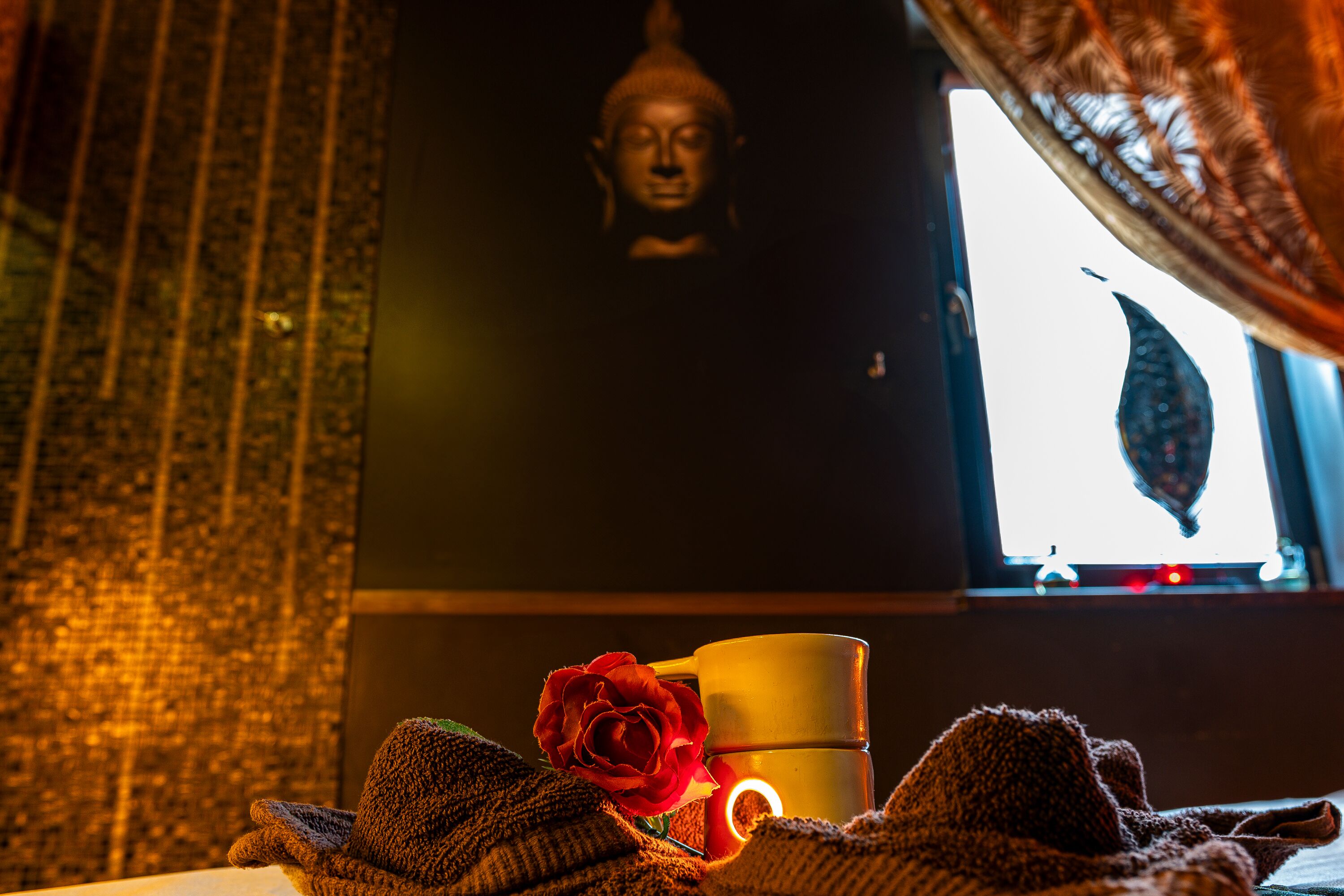 A room with a Buddha statue, a red rose, and a cup on a table.