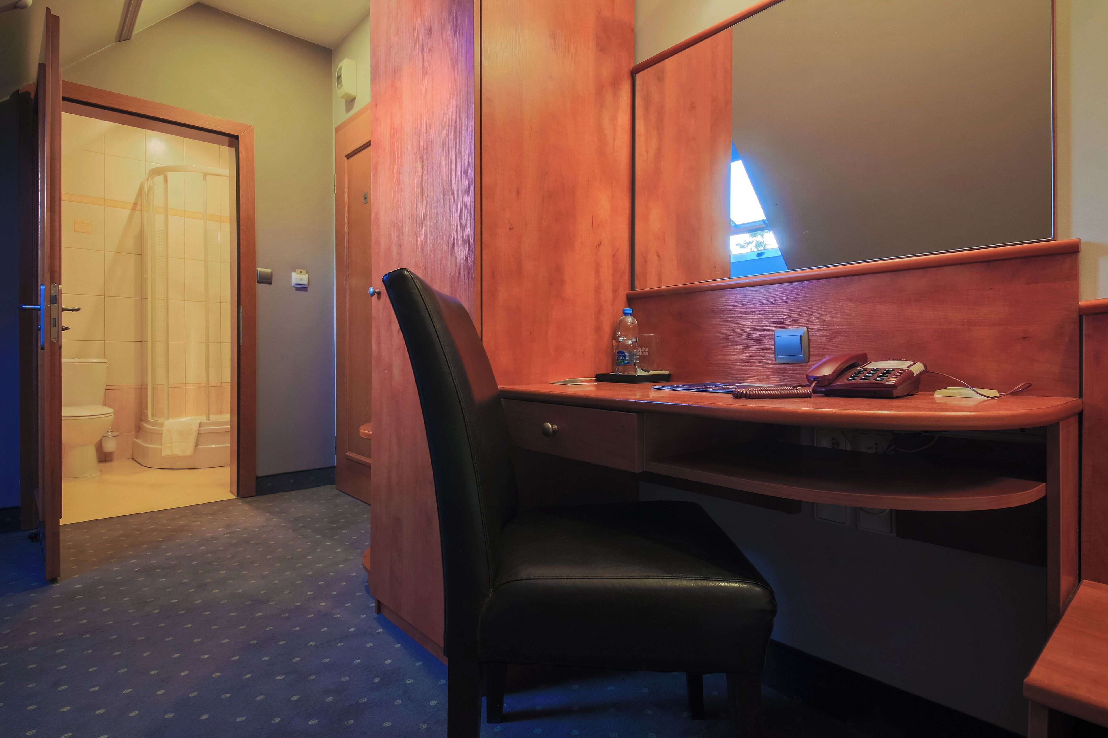 Een hotelkamer met een houten bureau, een zwarte stoel, een telefoon en een spiegel.